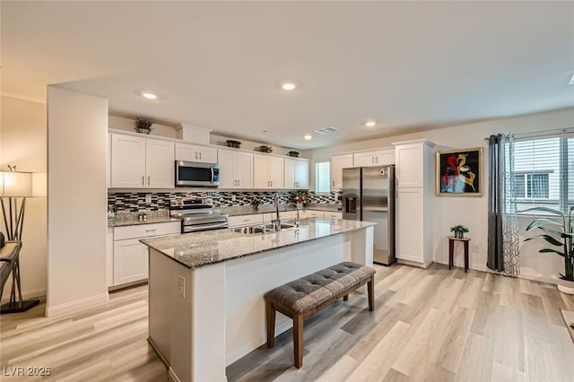 kitchen with a sink, backsplash, light wood-style floors, stainless steel appliances, and white cabinets