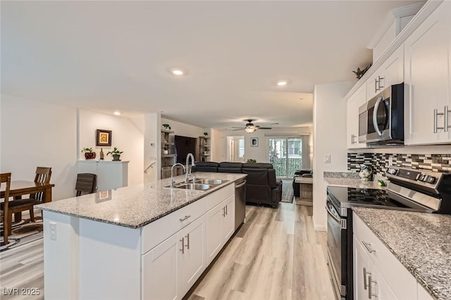 kitchen featuring a sink, open floor plan, light wood-type flooring, white cabinetry, and appliances with stainless steel finishes