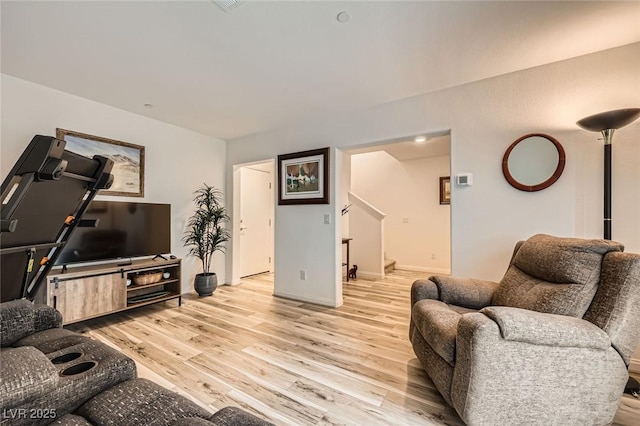 living area featuring baseboards, stairway, and light wood-style flooring