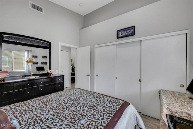 bedroom featuring light wood finished floors, a closet, visible vents, and a towering ceiling