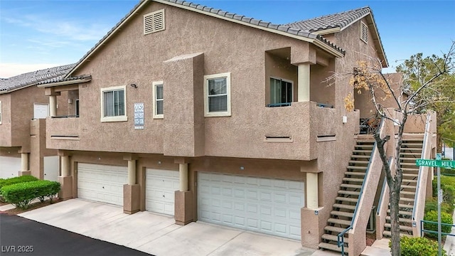 exterior space featuring stairs, driveway, a tile roof, a garage, and stucco siding