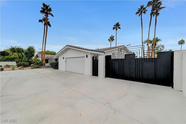 view of property exterior with fence, an attached garage, driveway, a tile roof, and stucco siding