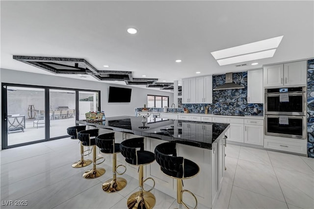 kitchen featuring double oven, wall chimney exhaust hood, a skylight, plenty of natural light, and recessed lighting