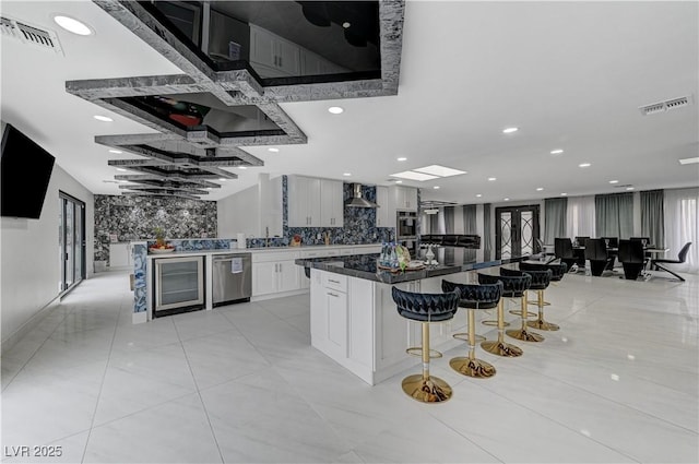 kitchen with stainless steel appliances, a kitchen bar, wall chimney range hood, a spacious island, and white cabinets