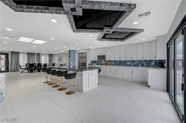 kitchen with appliances with stainless steel finishes, a breakfast bar, white cabinetry, decorative backsplash, and a large island
