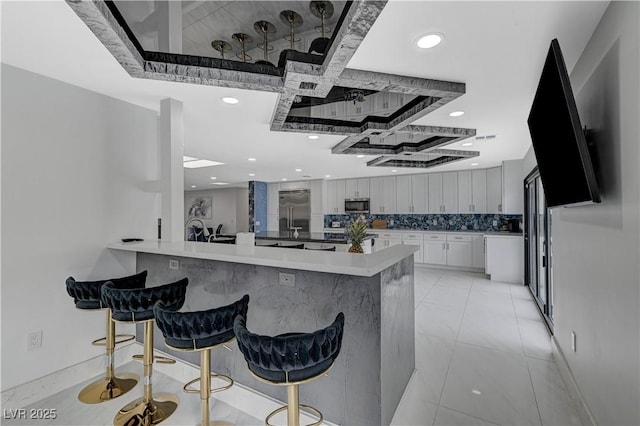 kitchen featuring appliances with stainless steel finishes, coffered ceiling, a breakfast bar, a peninsula, and recessed lighting