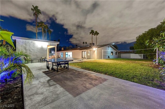 patio at twilight featuring volleyball court and a yard