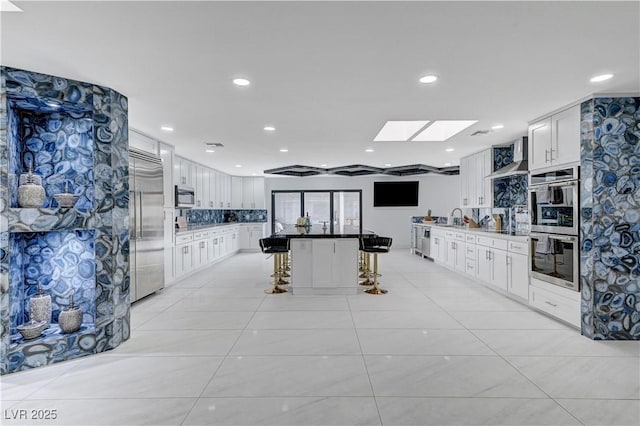 kitchen with stainless steel appliances, a breakfast bar, wall chimney exhaust hood, white cabinetry, and recessed lighting
