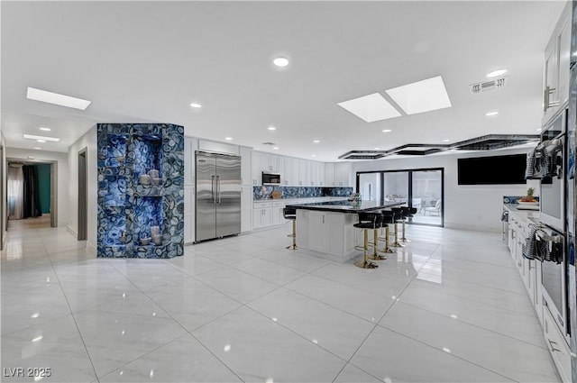 kitchen with appliances with stainless steel finishes, a skylight, a kitchen breakfast bar, white cabinets, and light tile patterned flooring