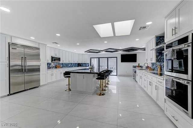 kitchen with stainless steel appliances, a kitchen breakfast bar, a sink, light tile patterned flooring, and white cabinets
