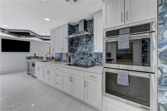 kitchen featuring stainless steel appliances, a sink, wall chimney range hood, light tile patterned flooring, and light countertops
