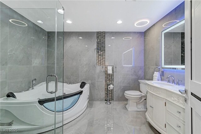 full bath with tile walls, marble tiled flooring, vanity, a tub to relax in, and toilet