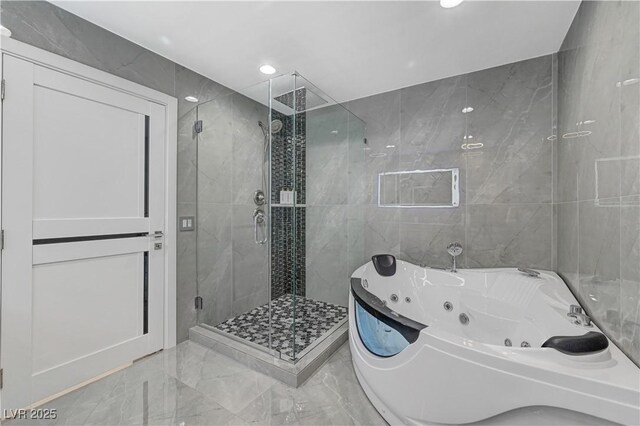 full bath with marble tiled floors, a tub with jets, a shower stall, tile walls, and recessed lighting