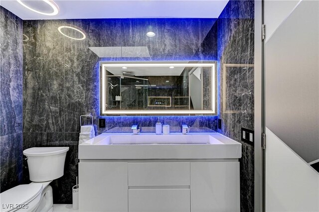 bathroom with tile walls, toilet, vanity, and a shower with door