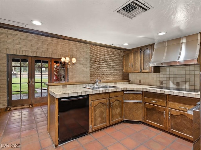 kitchen featuring tile counters, a sink, visible vents, wall chimney exhaust hood, and black appliances