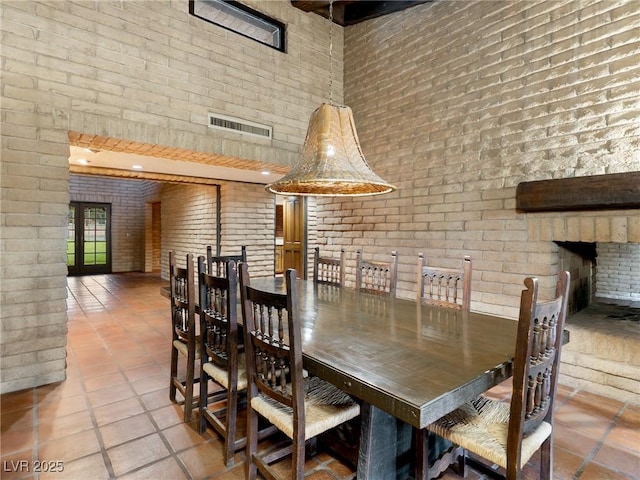 tiled dining area featuring brick wall, a towering ceiling, and visible vents