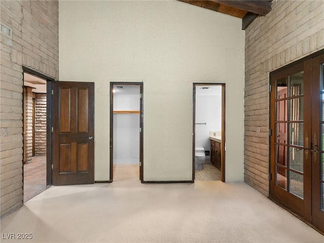 unfurnished bedroom featuring connected bathroom, french doors, a high ceiling, beamed ceiling, and a spacious closet