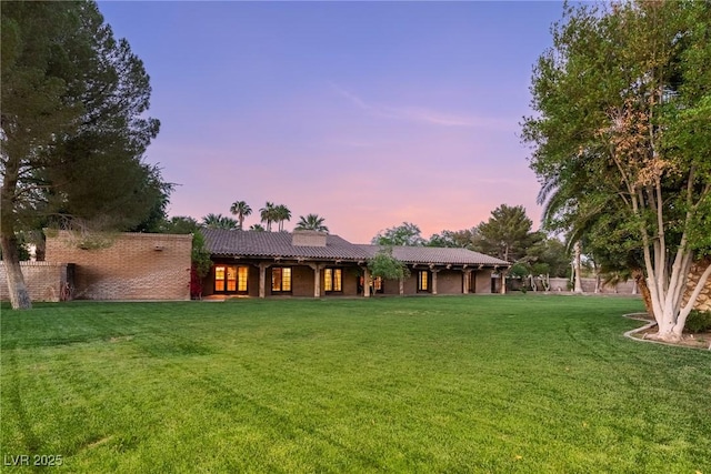 rear view of property featuring a tile roof, covered porch, and a lawn