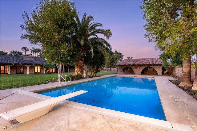 outdoor pool with a lawn, a patio area, and a diving board
