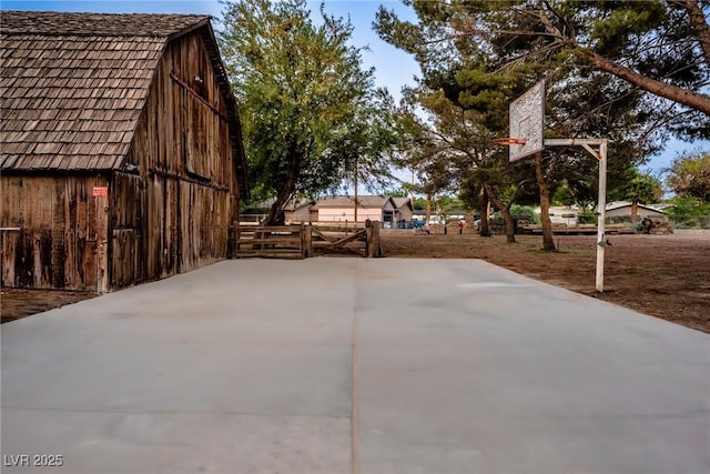 view of patio with fence, a barn, an outbuilding, and basketball hoop