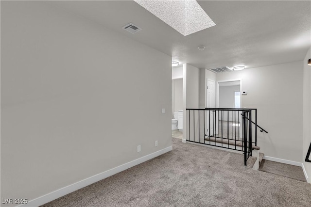 empty room featuring baseboards, carpet flooring, visible vents, and a skylight