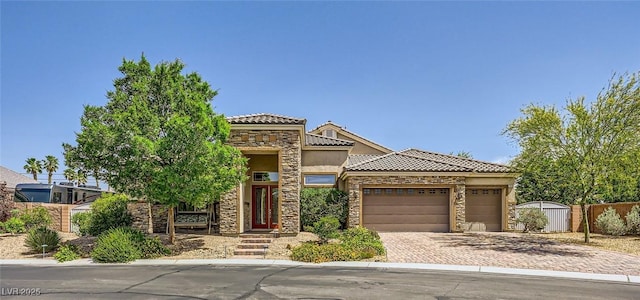 view of front of house featuring stone siding, a tile roof, fence, an attached garage, and decorative driveway
