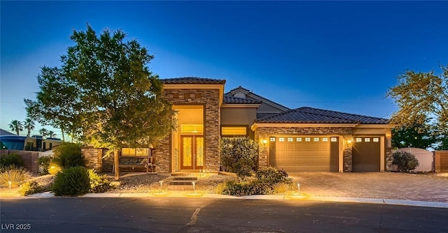 prairie-style house with stone siding, a garage, a tile roof, driveway, and stucco siding