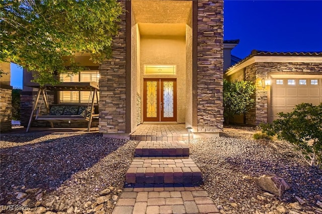 doorway to property with stone siding, a garage, and stucco siding