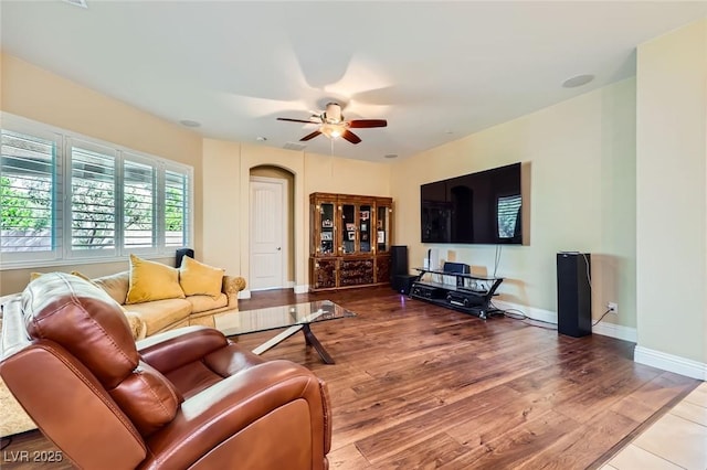 living area featuring ceiling fan, wood finished floors, baseboards, and arched walkways