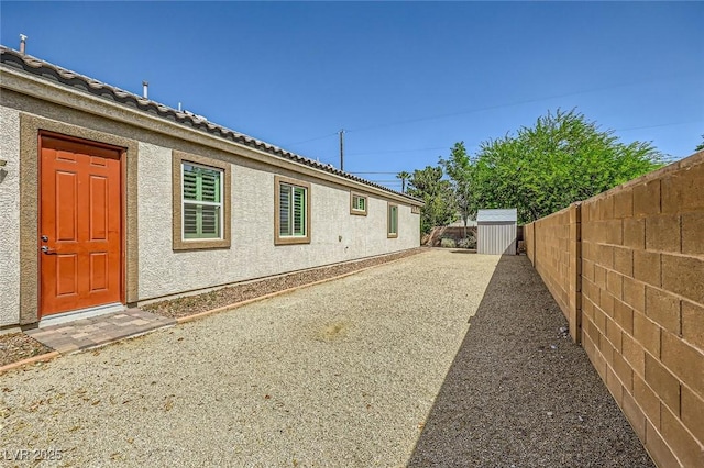 view of side of home with fence, a storage unit, an outbuilding, and stucco siding
