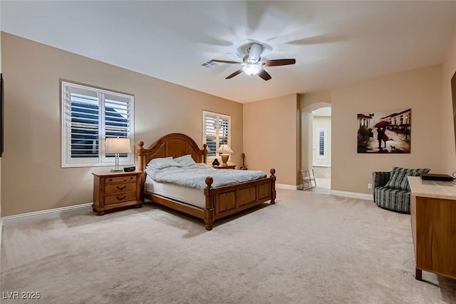 bedroom featuring arched walkways, light colored carpet, baseboards, and a ceiling fan