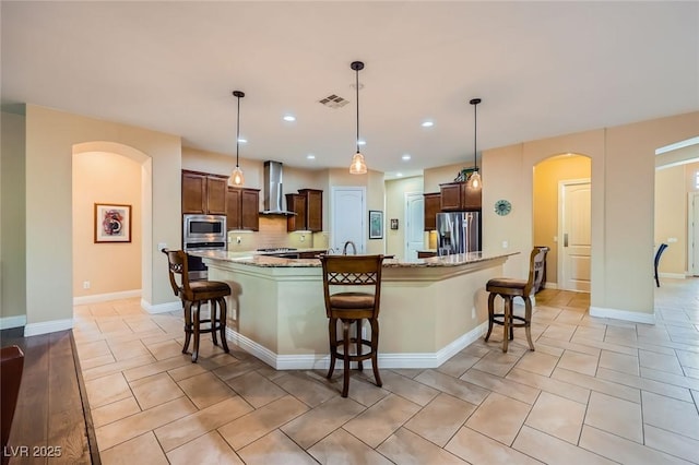 7418 Lawrence Powers Ct, Las Vegas, NV 89129 - kitchen featuring stainless steel appliances, wall chimney exhaust hood, arched walkways, a breakfast bar area, and light stone countertops