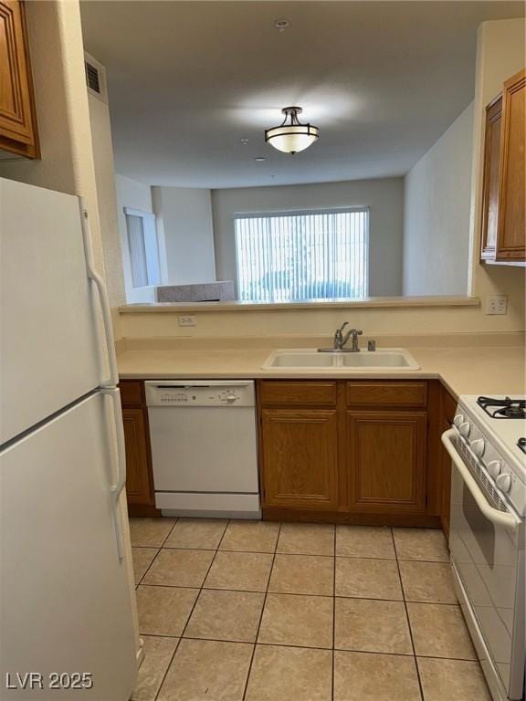 kitchen with brown cabinetry, light tile patterned flooring, a sink, and white appliances