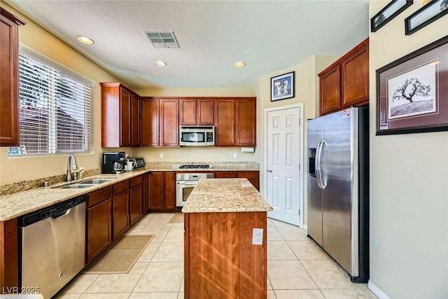kitchen with a sink, stainless steel appliances, light stone counters, visible vents, and a kitchen island
