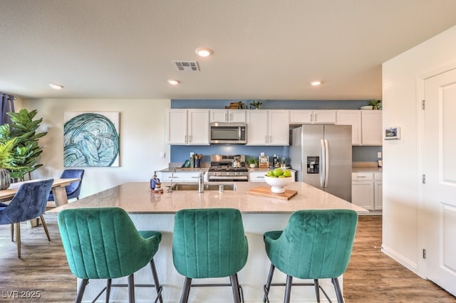 kitchen with a sink, stainless steel appliances, wood finished floors, visible vents, and white cabinets