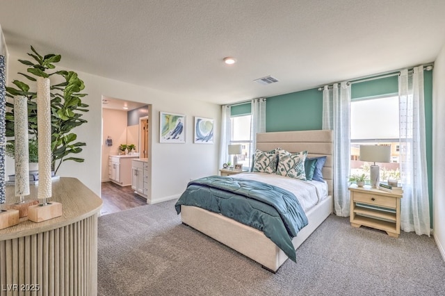 bedroom featuring a textured ceiling, carpet, baseboards, visible vents, and connected bathroom