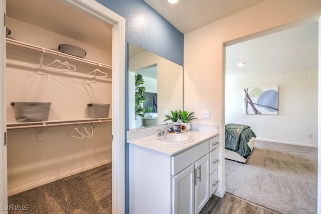 full bath featuring vanity, a walk in closet, and baseboards