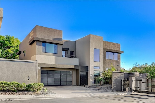 modern home with a gate, a garage, fence, concrete driveway, and a balcony