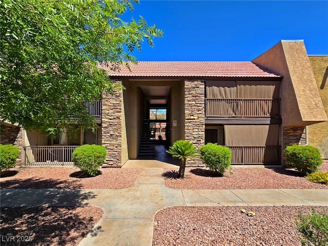 doorway to property with a tiled roof, stucco siding, stone siding, and a balcony