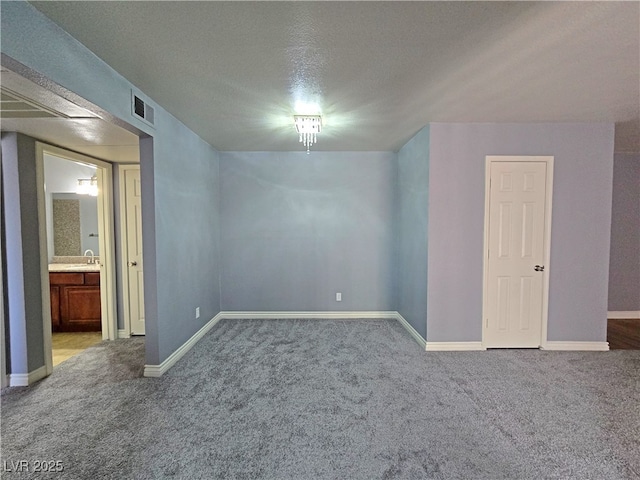 interior space with carpet floors, a textured ceiling, visible vents, baseboards, and ensuite bathroom