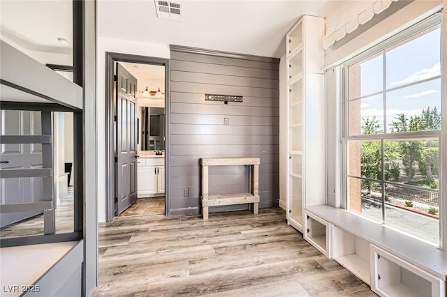 mudroom featuring light wood-type flooring, wood walls, and visible vents
