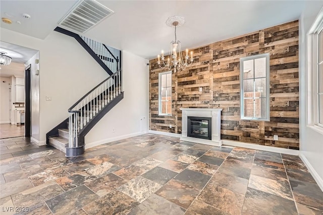 unfurnished living room featuring stairs, an inviting chandelier, and stone tile flooring