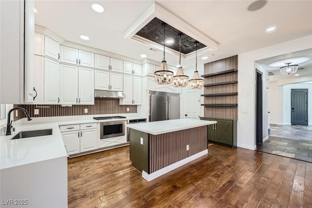 kitchen with a sink, stainless steel appliances, white cabinetry, under cabinet range hood, and a chandelier