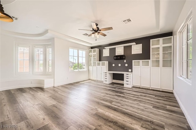 unfurnished living room featuring a tray ceiling, baseboards, ceiling fan, visible vents, and wood finished floors