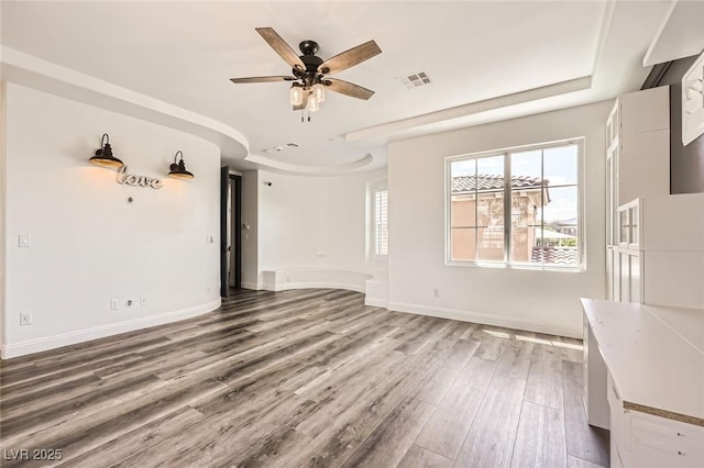 interior space featuring wood finished floors, visible vents, a ceiling fan, a raised ceiling, and baseboards