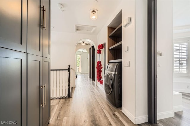 hallway featuring arched walkways, washer / clothes dryer, light wood-style flooring, and plenty of natural light