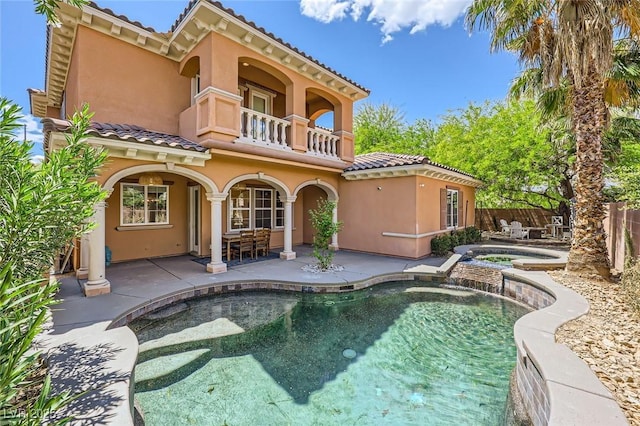 rear view of house featuring a balcony, fence, stucco siding, a tile roof, and an in ground hot tub