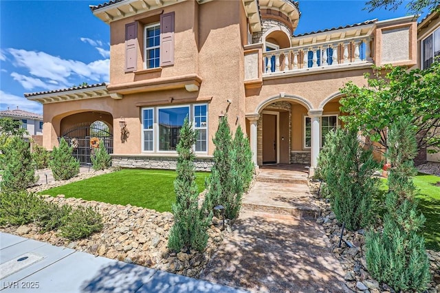 view of front facade with a balcony, stone siding, stucco siding, and a front yard