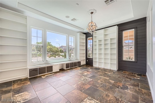 unfurnished dining area with a tray ceiling, visible vents, built in shelves, and a notable chandelier