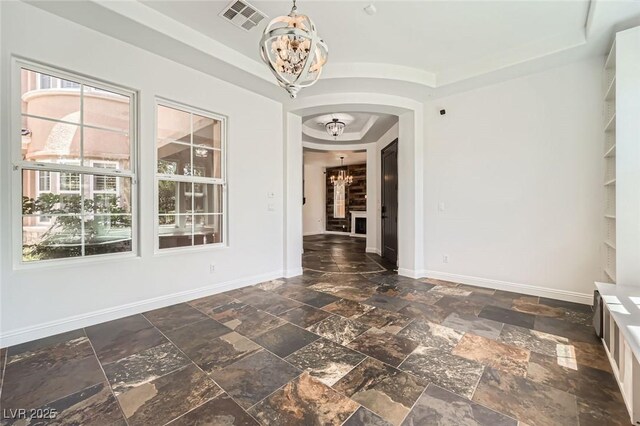 interior space featuring a tray ceiling, stone tile floors, an inviting chandelier, visible vents, and arched walkways